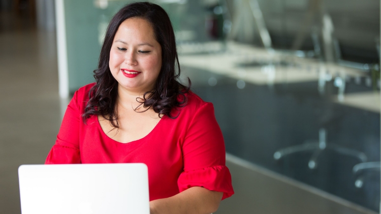 Smiling woman in office setting working on laptop, highlighting the ease of managing HSA benefits for future health expenses.