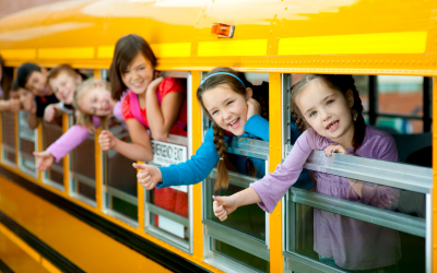 School-aged children leaning out of a yellow school bus, illustrating back-to-school season and family healthcare benefit planning.