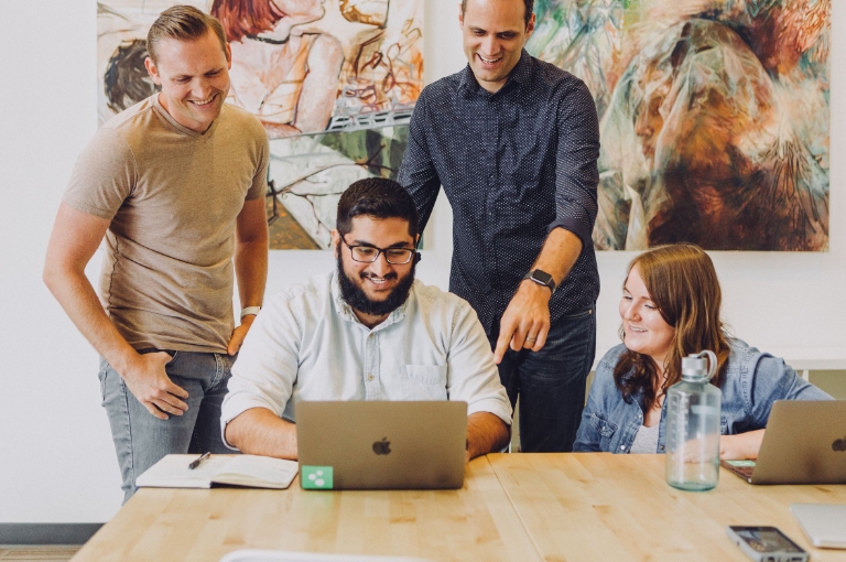Team collaborating around a laptop in a bright office, representing workplace communication and support with Health Savings Account toolkits and Eligible Expense Lists.