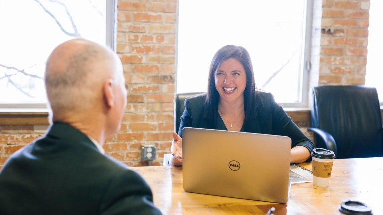 End-to-End COBRA Administration Smiling HR administrator providing end-to-end COBRA services support during a client consultation, seated at a conference table with a laptop.