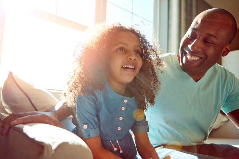 Father and daughter smiling together in a sunlit living room, representing family well-being supported by Flexible Spending Account communication toolkits.