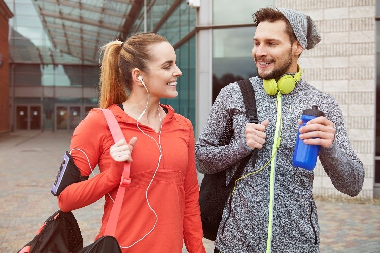 wo young adults dressed in activewear, carrying gym gear and headphones, highlighting how LSAs support physical wellness through gym memberships and workout gear reimbursements.
