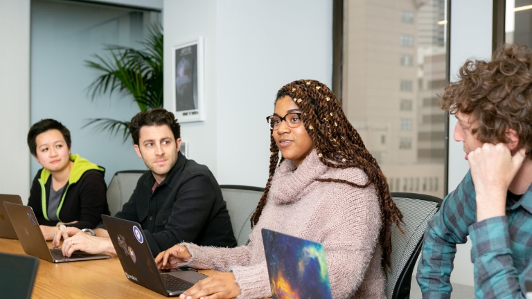 COBRA Open Enrollment Team meeting discussing COBRA Open Enrollment Services, with diverse professionals collaborating on laptops in a modern office setting.