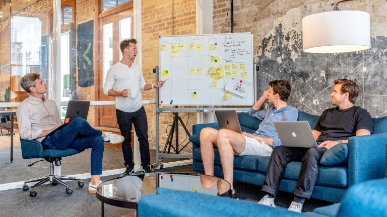 Team collaborating in a modern office, reviewing plans on a whiteboard during a strategy meeting.