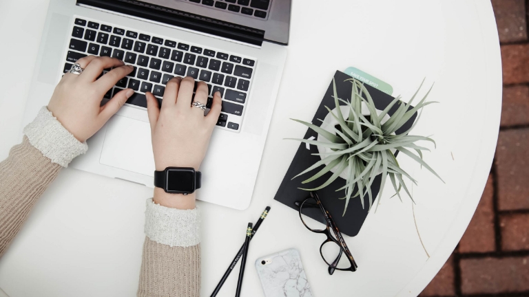 Hands typing on computer keyboard beside notebook, glasses, and phone, highlighting technology-driven Billing Services Reporting.