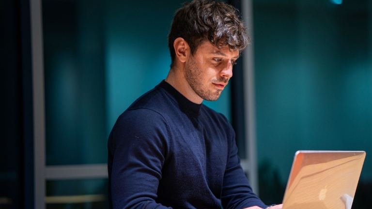 COBRA Reporting Young professional in dark sweater reviewing detailed COBRA service reports and benefits data on a laptop in a quiet office.