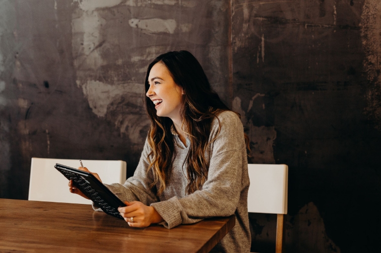 A professional with long hair sits at a wooden table, holding a tablet and pen while smiling in a modern office setting. The scene emphasizes the importance of using your summary plan description as an accessible employee resource for understanding workplace benefits and making informed decisions.
