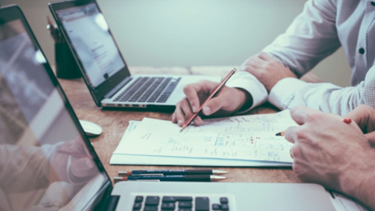 Business team analyzing paperwork with laptops,ymbolizing Premium Only Plans compliance support for employers and HR teams.