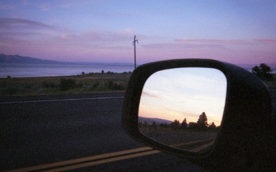 A scenic road at sunset with a car’s side mirror reflecting the path behind — symbolizing the need to look back and clarify benefit misconceptions before moving forward.