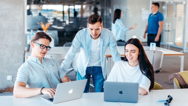 Three employees gathered around laptops in an open office, representing seamless coordination between HRAs, HSAs, and FSAs for personalized financial wellness.